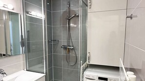 A modern bathroom with a glass-enclosed shower, a Bosch washing machine, and a white sink with a mirror.