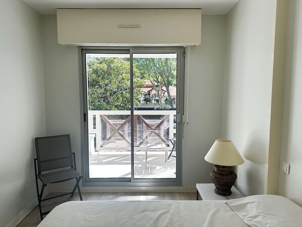 Habitación de hotel con cama, una silla, una lámpara y una puerta corredera de vidrio que da a un balcón exterior.