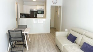 A compact living space with a kitchenette, a dining area with a table and chairs, and a sofa with cushions.