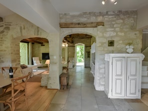 Un intérieur rustique avec des murs en pierre apparentes, des meubles en bois et une arche centrale qui mène à un espace extérieur lumineux.