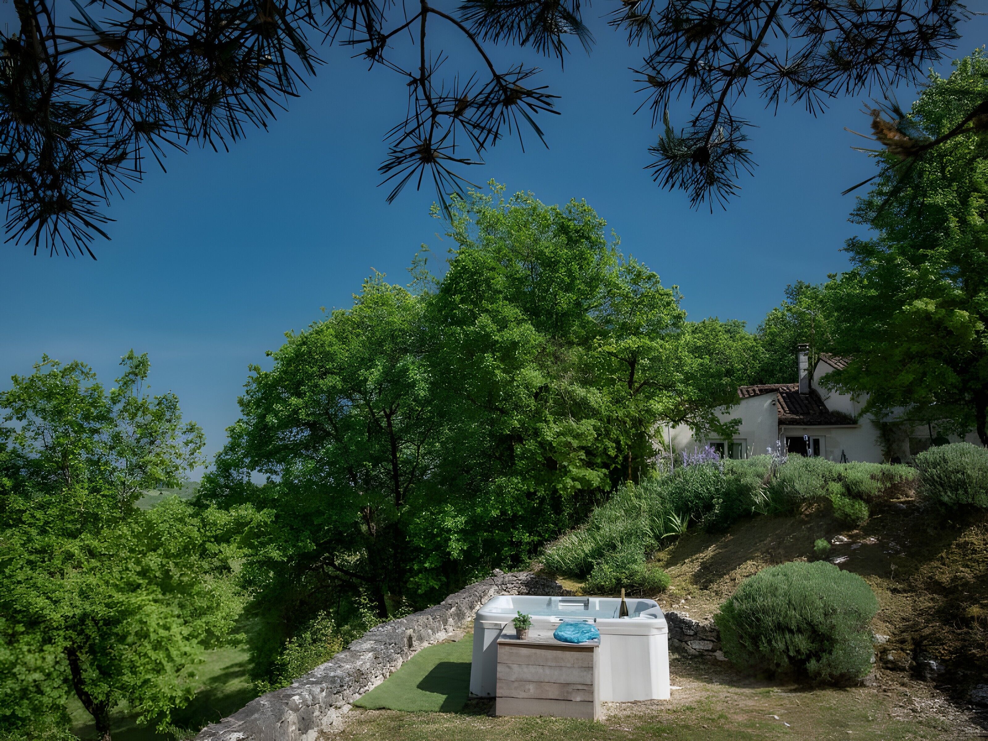 A house with a stone wall, a hot tub, and lush greenery.