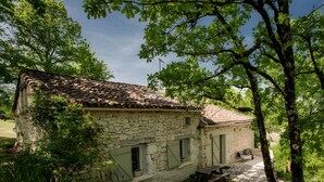 A stone building with a tiled roof, surrounded by greenery and trees. - Charming Cottage in Fargues (Prayssac/Montcuq) — Private Pool & Spa, Vineyard View (BAGAT EN QUERCY)
