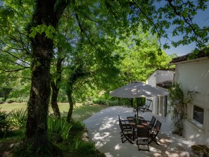 Eine Außenpatio mit Tisch und Stühlen, umgeben von viel Grün und einem weißen Gebäude.