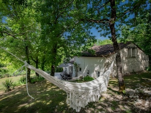 Un hamac dans un jardin luxuriant et verdoyant, avec un bâtiment en pierre en arrière-plan.