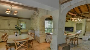 A rustic kitchen with wooden furniture, stone walls, and a dining area with a large table and chairs. - Charming Cottage in Fargues (Prayssac/Montcuq) — Private Pool & Spa, Vineyard View (BAGAT EN QUERCY)