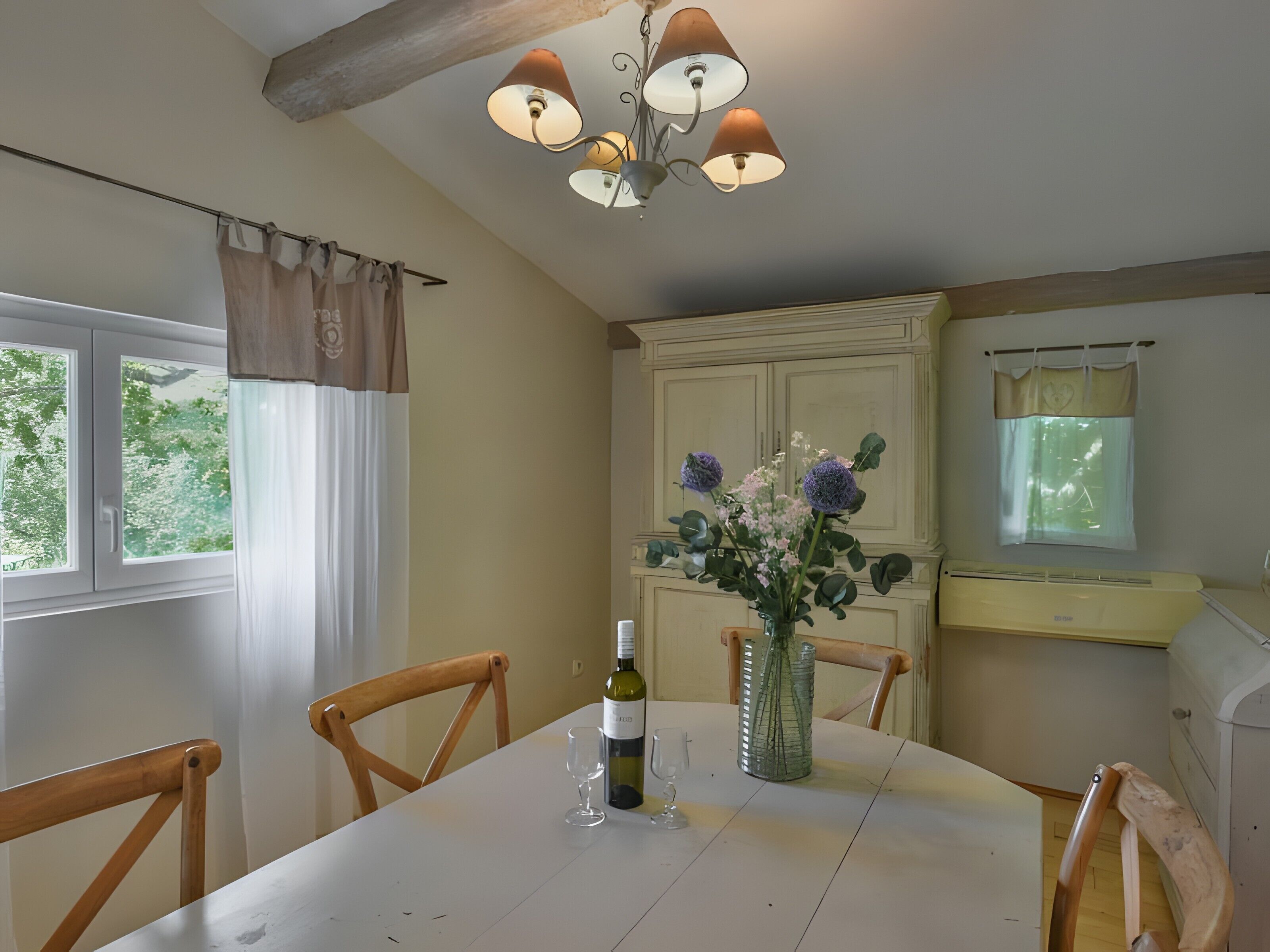 A dining area with a table, chairs, a chandelier, a cabinet, and a window with curtains.