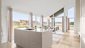Une cuisine moderne dotée d’un îlot central, de grandes fenêtres et offrant une vue sur l’extérieur.