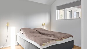 Une chambre à coucher avec un lit, deux lampes de chevet, une fenêtre avec des stores et un plancher en bois.