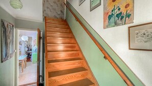 A wooden staircase with a handrail, leading to a room with a green wall and various framed artworks.