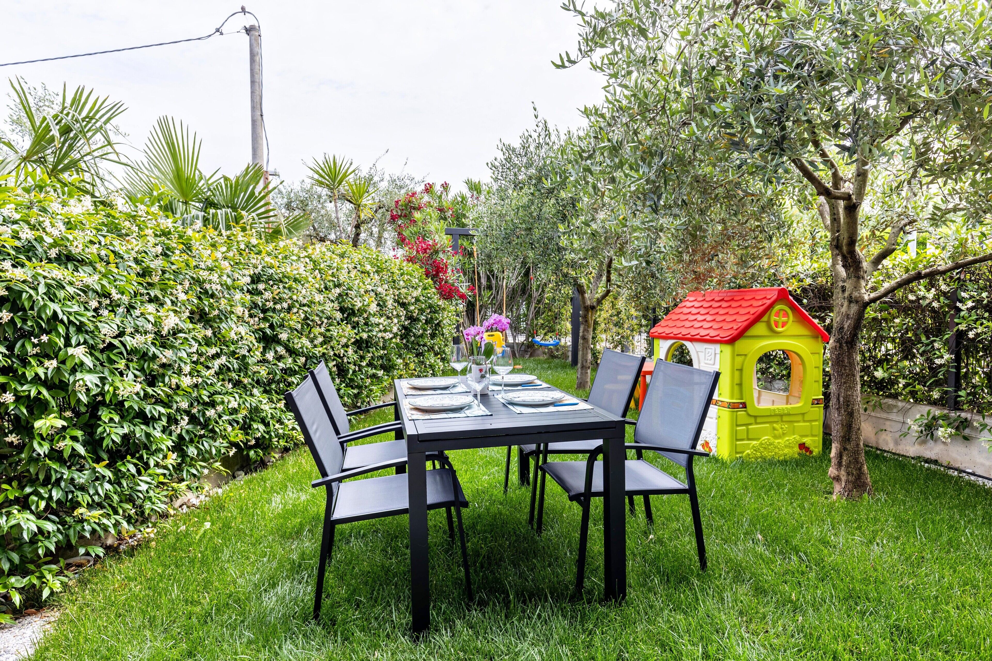 A garden with a table and chairs, a small playhouse, and various plants.