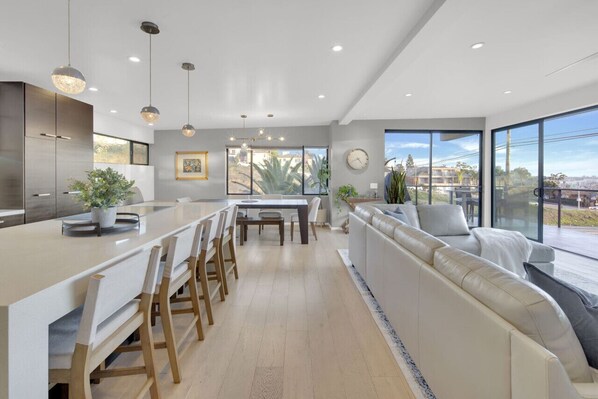 A modern kitchen with a central island, dining area, and a seating area with a view.