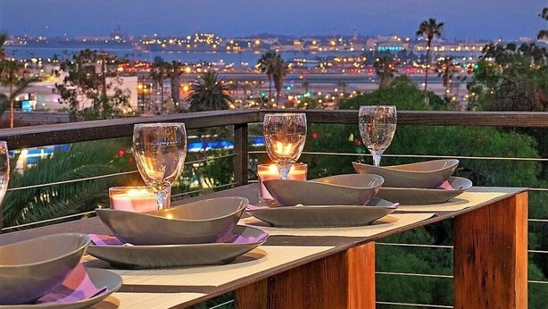 A table set with wine glasses and bowls, overlooking a cityscape at dusk. - The Gem of Mission Hills: Luxury 5BR Home with Luxe Amenities and views` (San Diego)