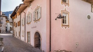 Un bâtiment rose avec des fenêtres en arc de cercle et une porte, une rue pavée et un portail en métal.