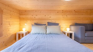 A wooden-paneled room with a bed, two bedside tables with lamps, and a grey sofa.