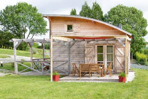 A wooden cabin with a covered porch, a table and chairs, and two potted plants. - Chalet '5 Pers Landeleau 2kms Canal' with Private Terrace and Shared Garden (Landeleau)