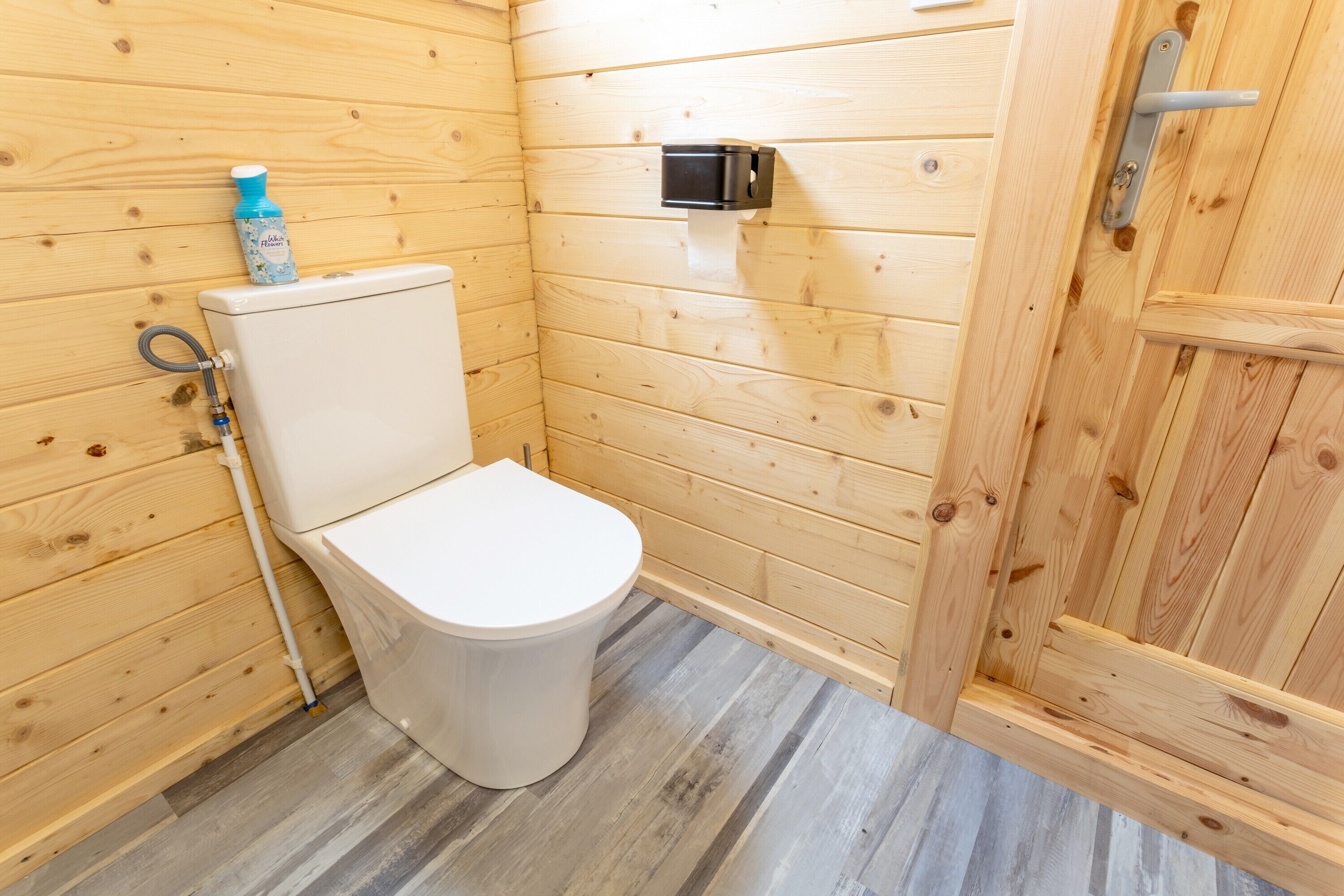 Ein Badezimmer mit Holzwandverkleidung, einer weißen Toilette, einem Seifenspender und einem Handtuchhalter.