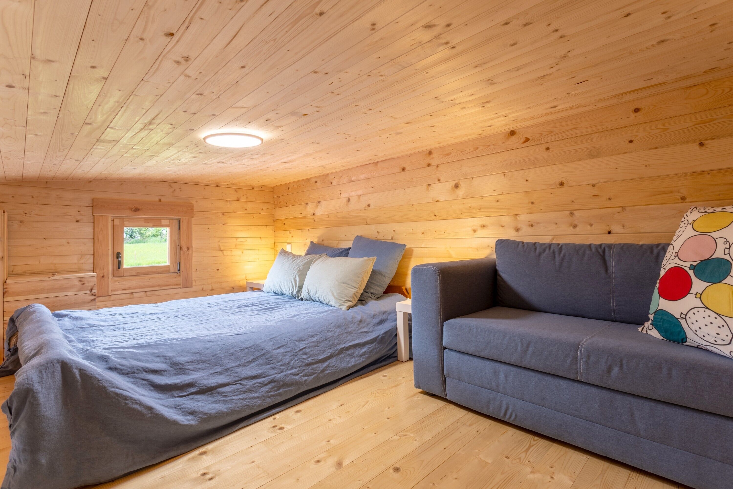 Ein Zimmer in einer Holzhütte mit einem Bett, einer Couch und einem Fenster.