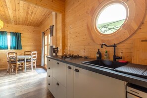 A wooden interior with a round window, a kitchen area with a sink, and a dining table with chairs.