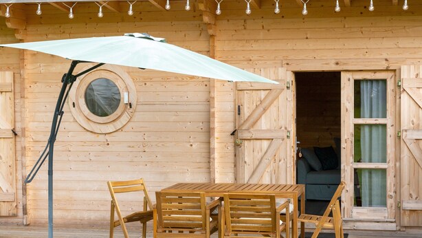 Eine Holzhütte mit einem Rundfenster, einem Tisch mit Stühlen und einem Sonnenschirm.