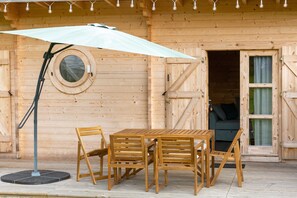 A wooden cabin with a round window, a table with chairs, and an umbrella.