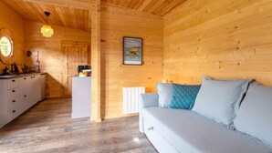 Ein Holzblockhaus-Innenraum mit Küchenzeile, einer Couch mit Kissen, einem gerahmten Bild an der Wand und einem Fenster.
