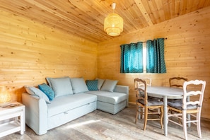 A wooden cabin interior with a light-colored sofa, a dining table with chairs, and a hanging light fixture.