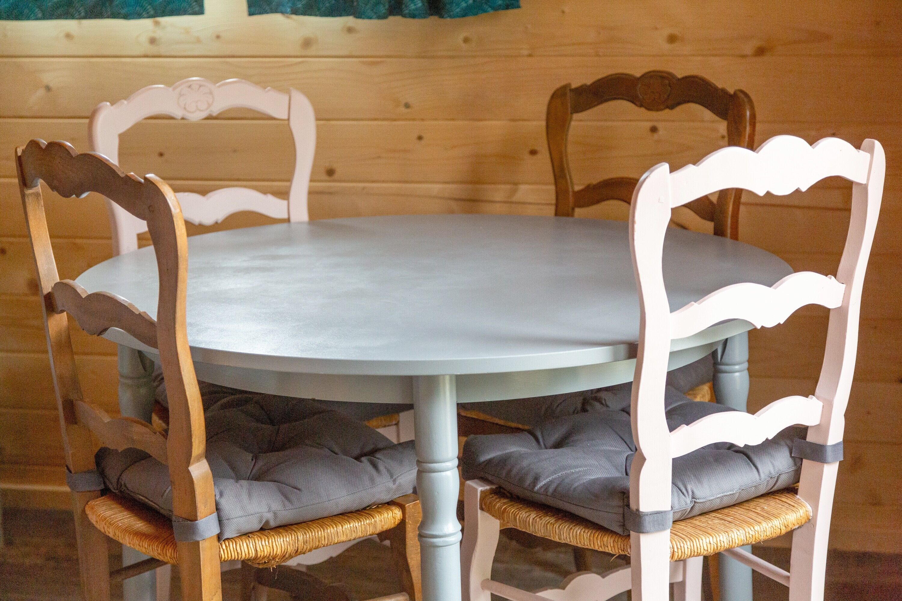Ein runder Tisch mit vier Stühlen, jeder mit einer Sitzkissen. Die Stühle haben einen Holzrahmen und eine weiße Oberfläche.