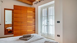 A bedroom with a bed, a wooden wardrobe, a mirror, and a window with curtains. - Apartment 'Casa Batistei Ribes' with Lake View, Balcony and Wi-Fi (Molveno)