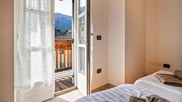 A bedroom with a bed, a window with curtains, and a view of a balcony. - Apartment 'Casa Batistei Ribes' with Lake View, Balcony and Wi-Fi (Molveno)