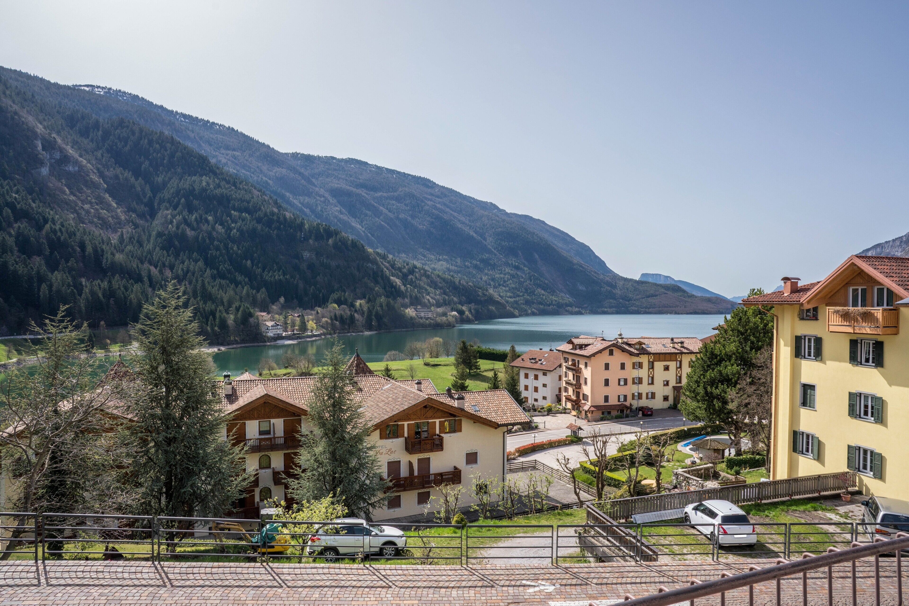 A mountain-view hotel with multiple balconies, a parking area, and a view of a lake.