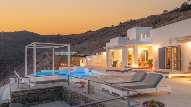 Uma villa moderna com piscina, área de estar externa e vista para as colinas ao redor.