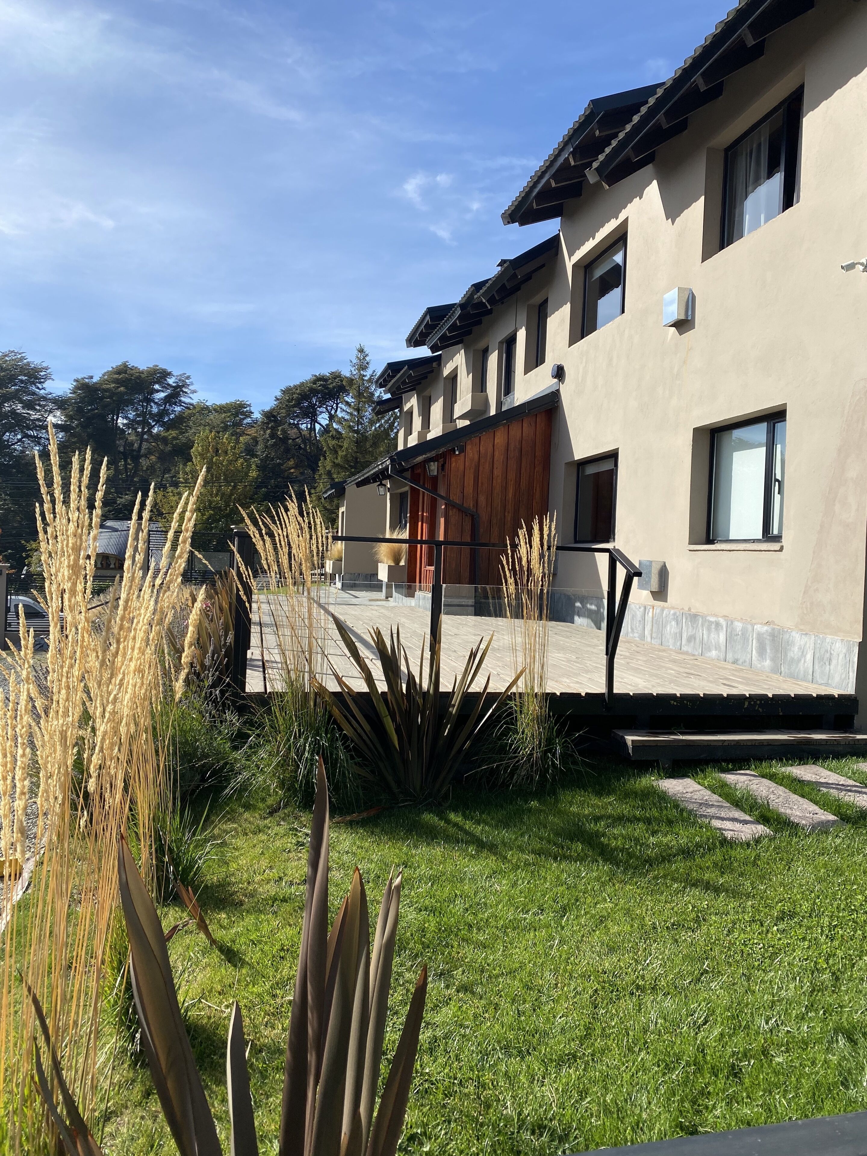 Una casa moderna con techo plano, amplios ventanales y un césped cuidado con hierbas altas y un pequeño jardín.