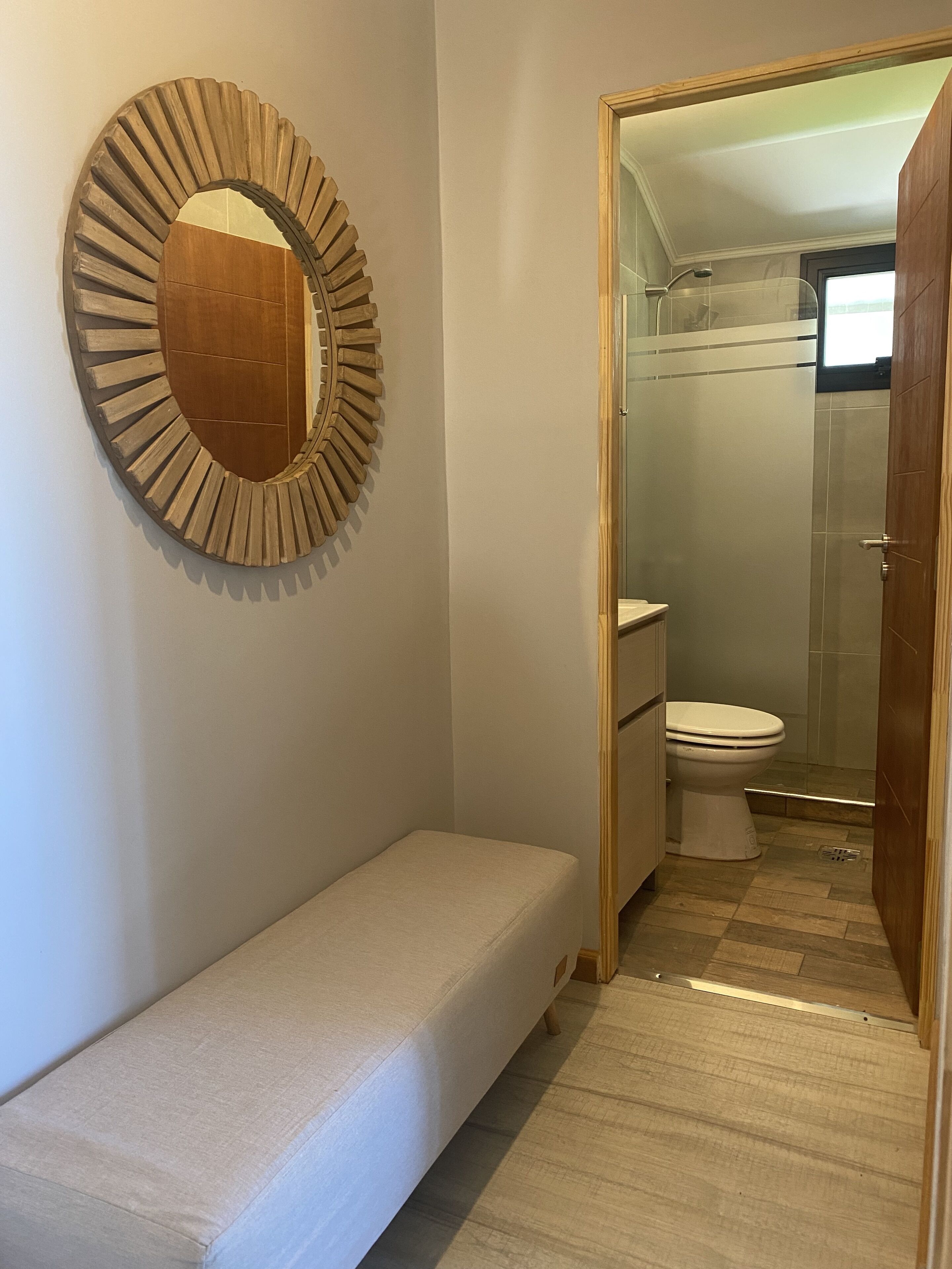 A small, compact bathroom with a shower, toilet, and a bench.