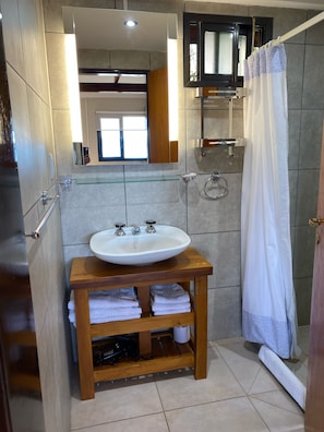 A bathroom with a wooden vanity, a white sink, and a glass shelf. - Quillaipe Apart Suite (San Carlos de Bariloche)