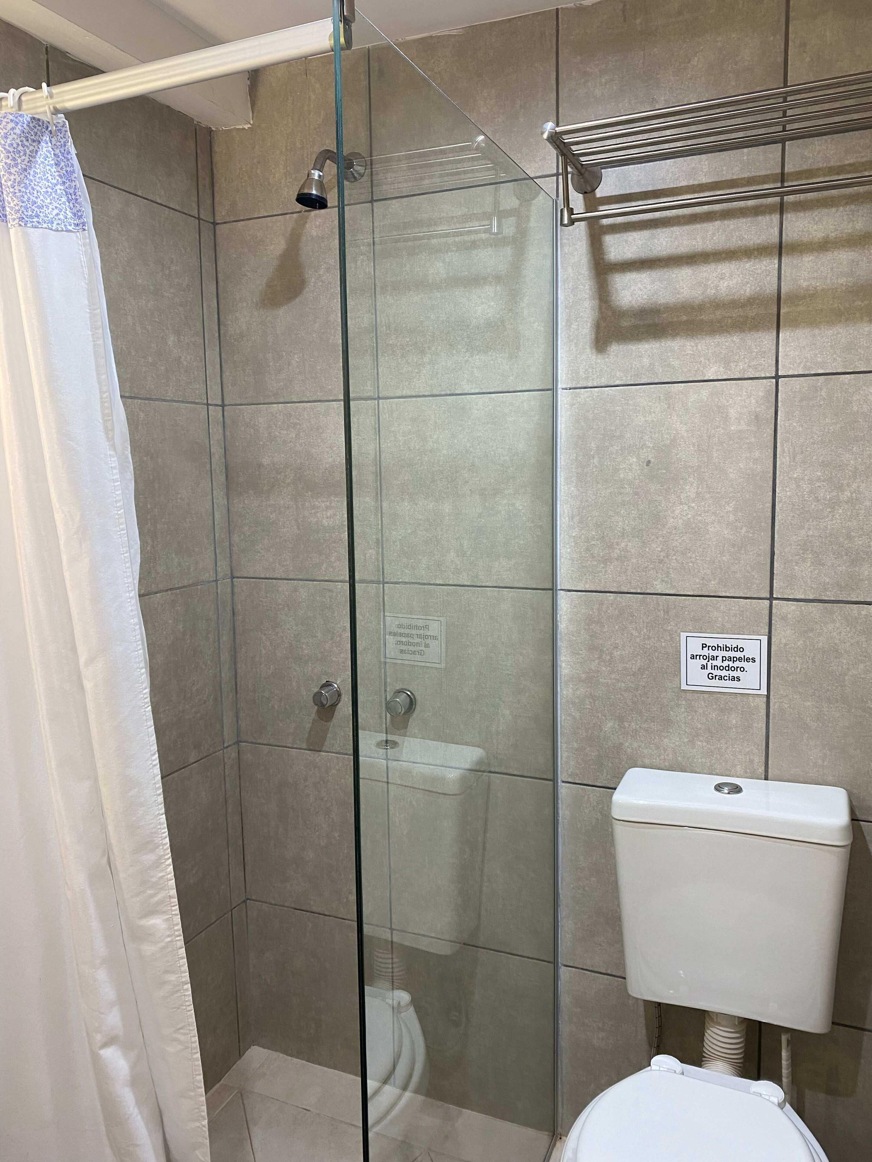 Et bruseområde med glasvægge, et toilet og en håndklædeholder.