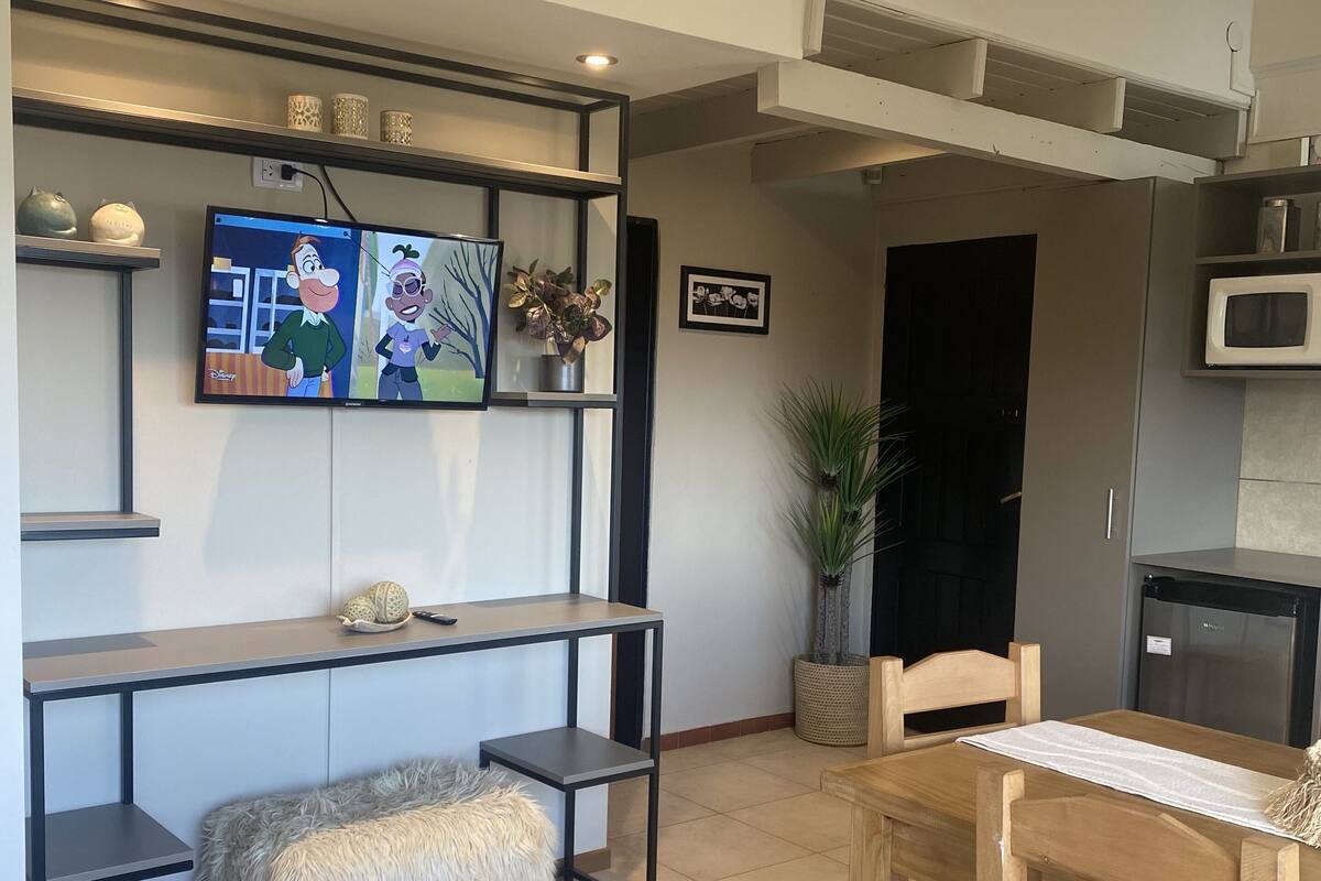 Una sala de estar moderna con televisor, una mesa de comedor de madera, un sofá y una pequeña cocina.
