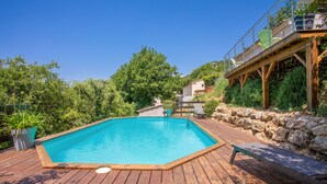Une terrasse en bois avec une piscine, un mur en pierre et un escalier en bois menant à un balcon.