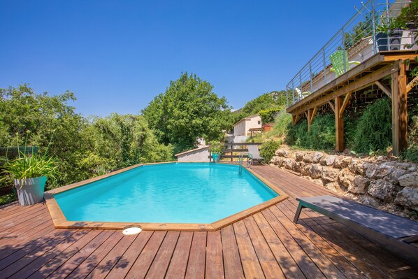 Une terrasse en bois avec une piscine, un mur en pierre et un escalier en bois menant à un balcon.