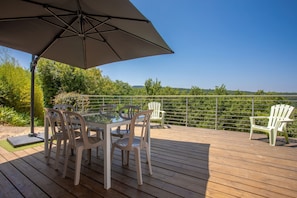 Une terrasse avec une table et des chaises, un parasol et une vue sur les arbres et les collines.