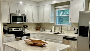 A modern kitchen with white cabinetry, a stainless steel refrigerator, a built-in microwave, and a central island with stools.