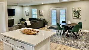 A modern living room with a sofa, a dining table with chairs, and a kitchen area with a countertop and cabinets.