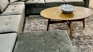 A modern living room with a sectional sofa, a round coffee table, and a dining area with a small table and chairs.