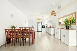 Una cocina moderna con armarios blancos, un comedor con sillas de madera y una lámpara colgante.