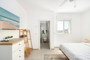 Un dormitorio con cama, cómoda de madera, televisor y vista de la ciudad a través de una ventana.