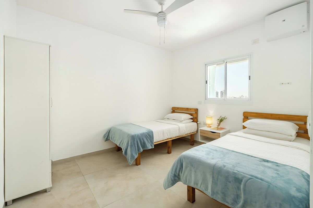A bedroom with two single beds, a wardrobe, a ceiling fan, and a window with a view.