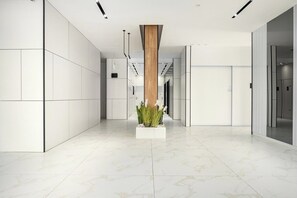 A modern interior with a central column, white tiled walls, and a marble floor.