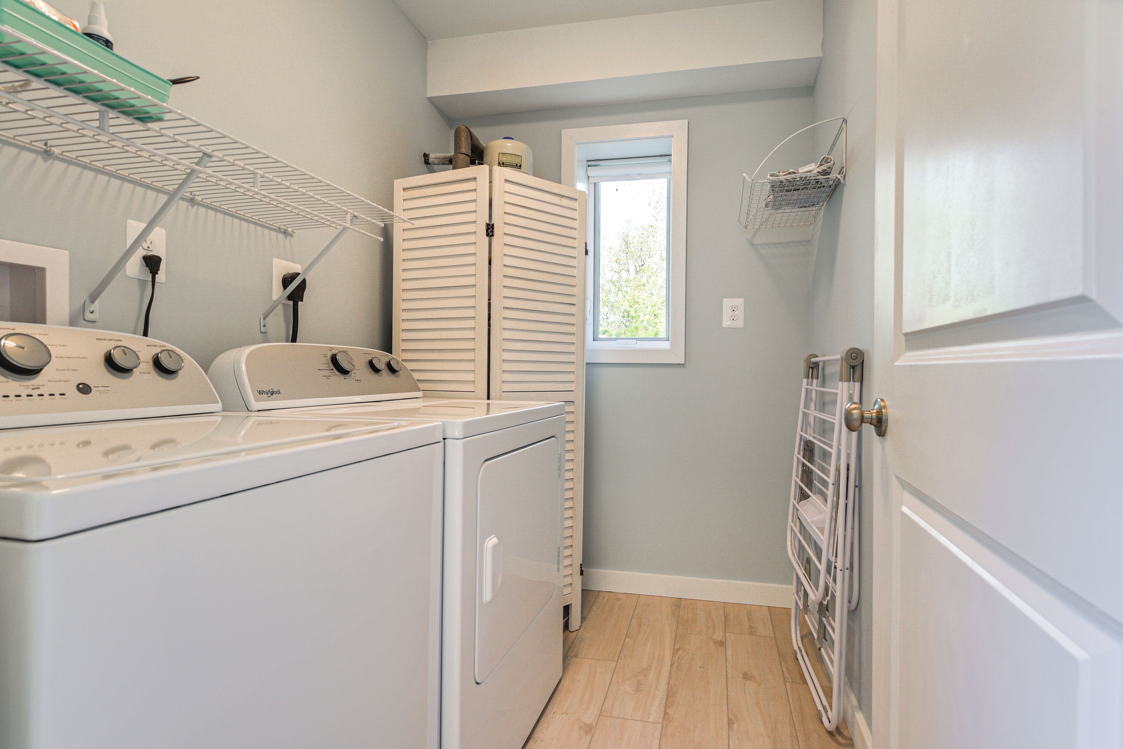 A laundry room with stacked dryers, a drying rack, and a window providing natural light.