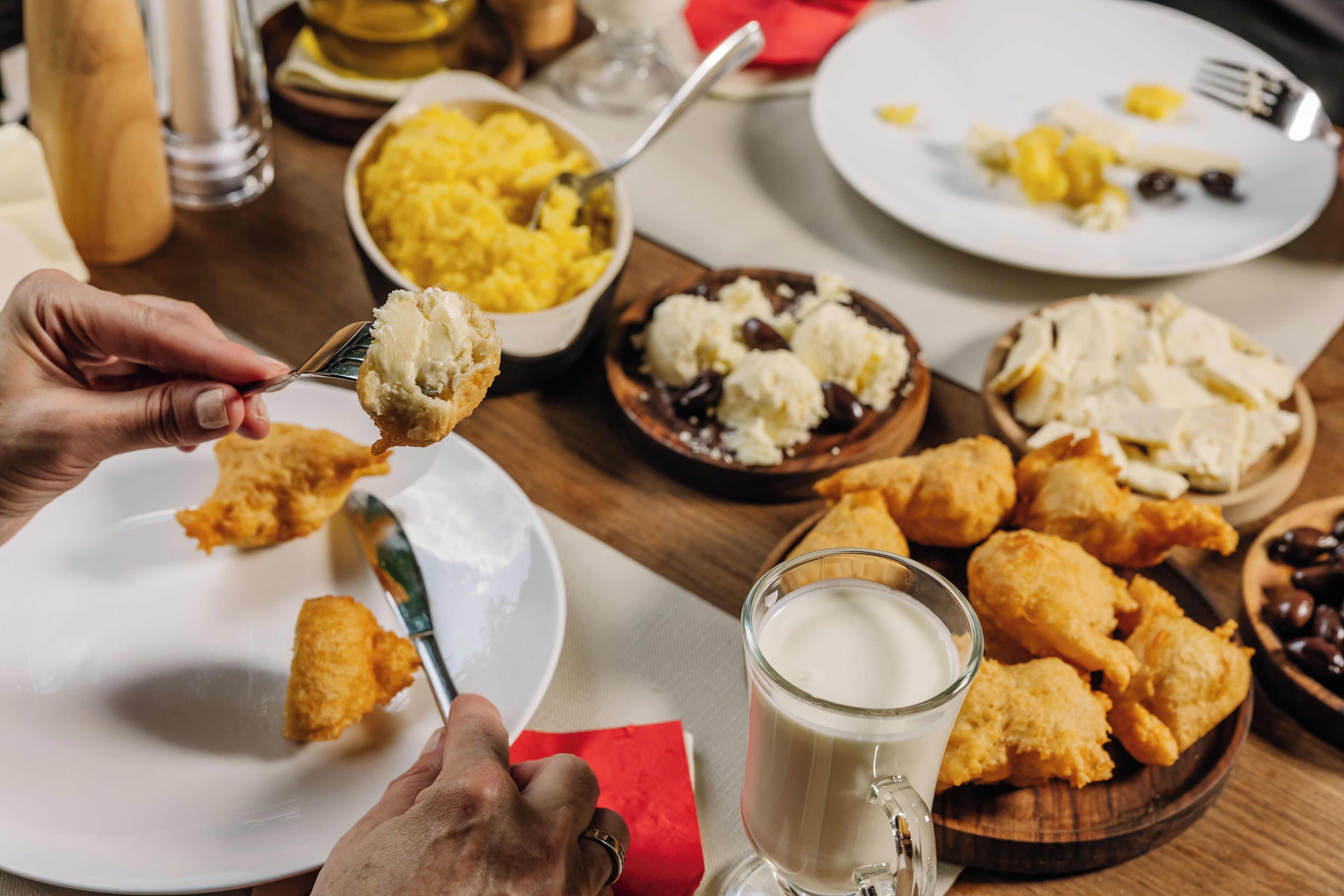 A dining table with various food items, including a bowl of yellow food, a plate with a fork, and a glass of milk.
