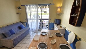 Ein kleiner Wohnbereich mit einer Couch, einem Esstisch für zwei Personen, einem Fernseher und einem Fenster mit Vorhängen.