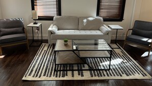 A living room with a grey sofa, two armchairs, a glass coffee table, and a patterned rug. - Pet Friendly Spacious Luxe Corner House for Professionals - Left Side (Kingston)